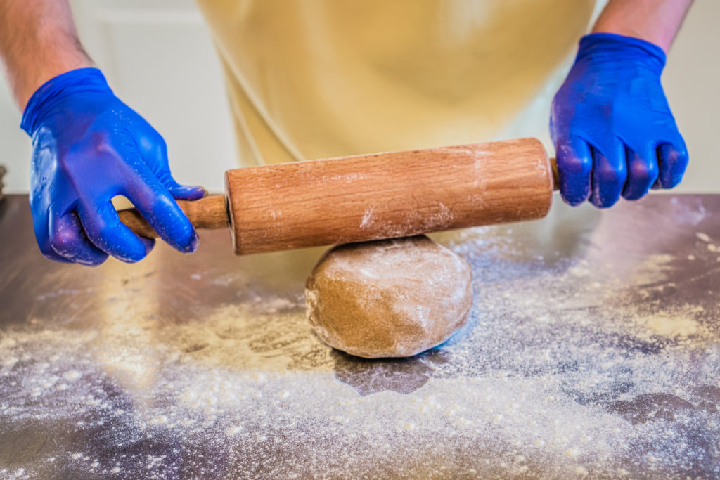 A men's hands in gloves preparing dough with rolling pin